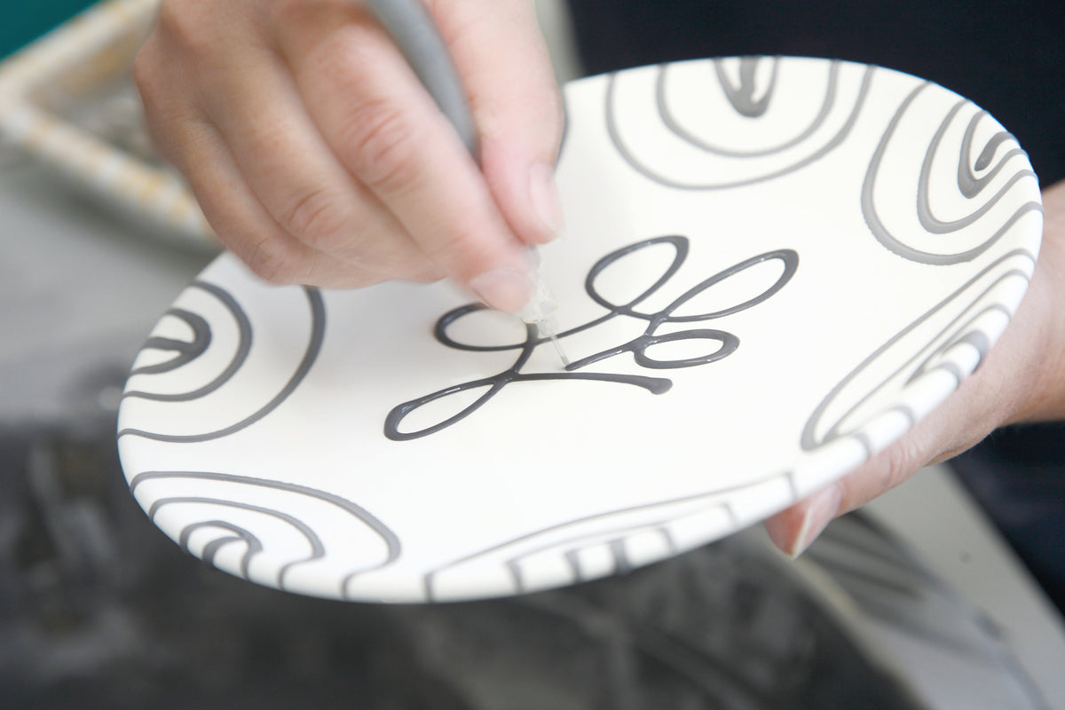 Person holding a small ceramic plate with decorative black patterns