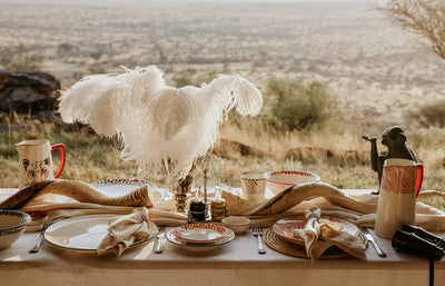 Gmundner Lodge. Dining table set with plates, cups, and a decorative feather centerpiece in a natural setting.